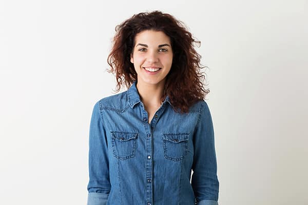young pretty woman with natural curly hairstyle smiling, positive emotion, happy, isolated on white background, denim blue shirt, hipster style, student, looking in camera